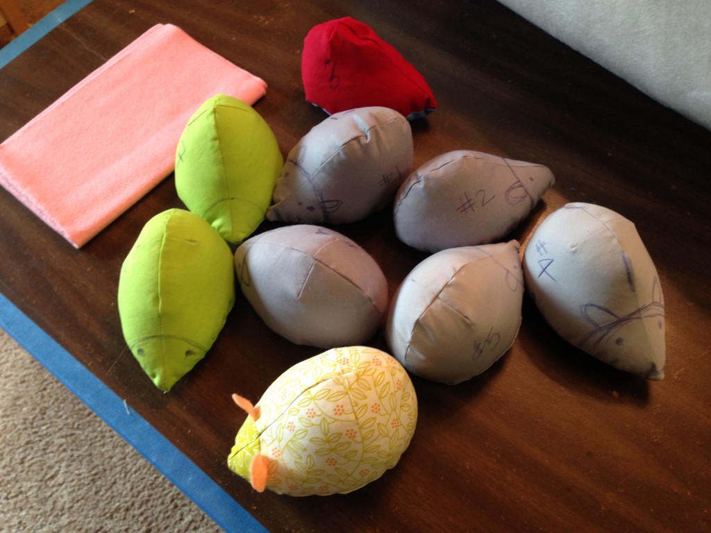 Nine prototypes of the Hedgie pincushion sit on a wooden table top.  