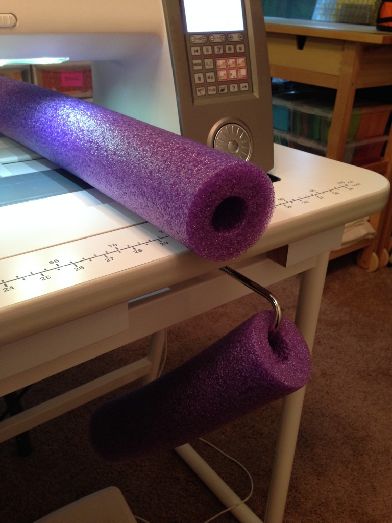Purple pool noodle has been threaded on a knee lift of a sewing machine. 