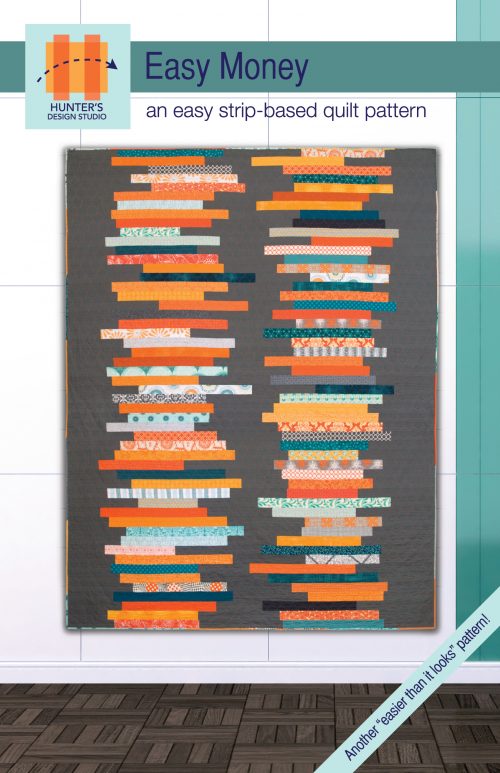Image is of the Easy Money quilt hung up on the wall. The quilt uses strips of oranges, blues and whites arranges in an improvisational stacked coins pattern