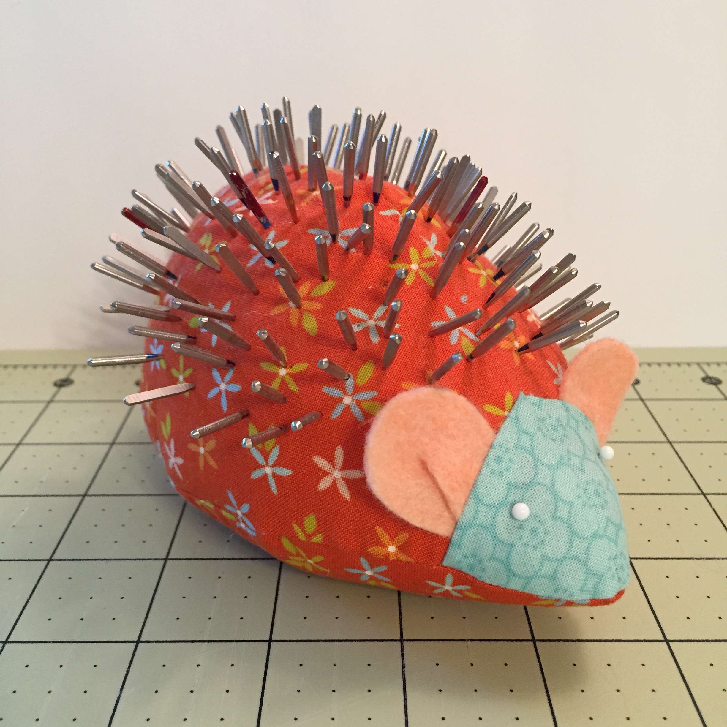 Hedgie Pincushion made with orange fabric is full of used sewing machine needles.