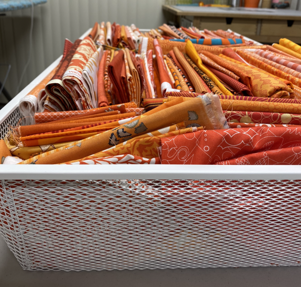 White wire drawer filled with various cuts of orange fabrics. 