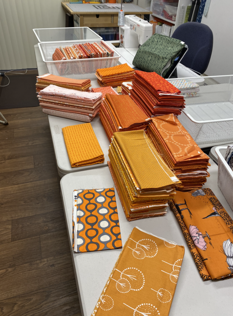 White wire baskets sitting on a table, half empty with orange fabric cuts being refolded on the table. 