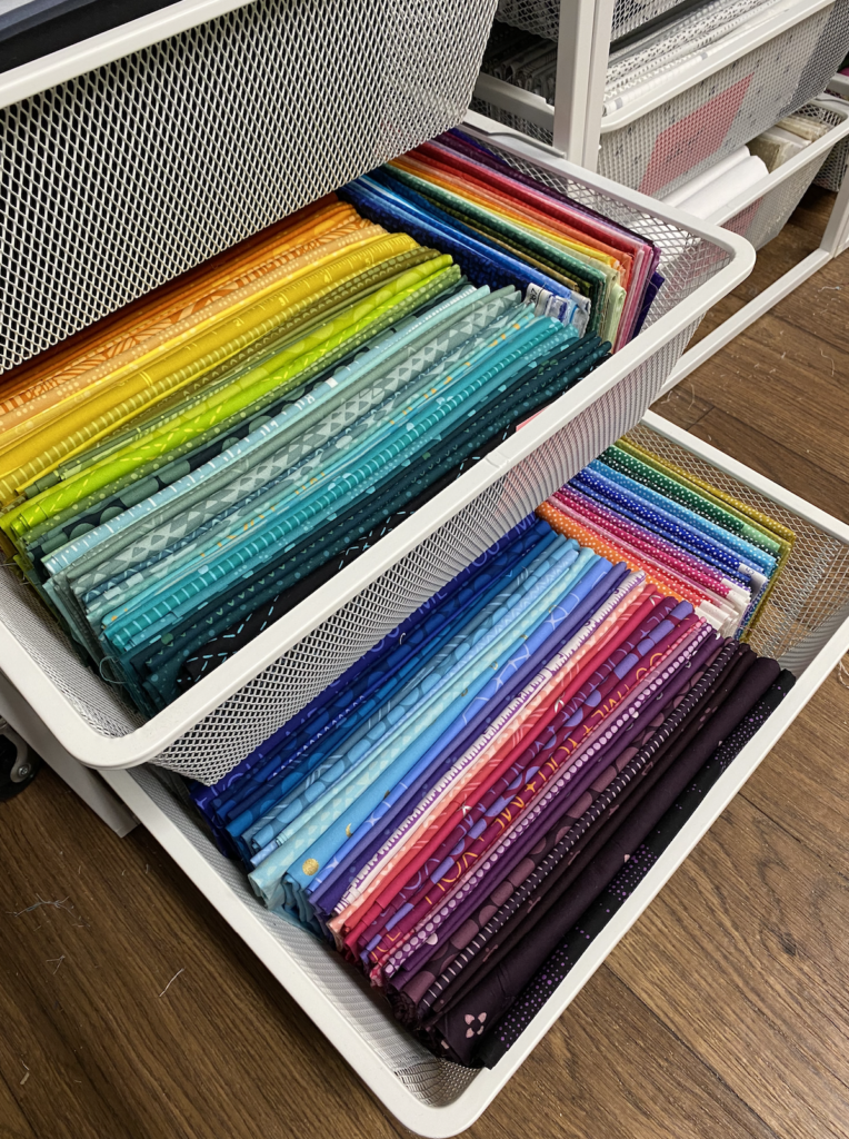 Freely moving white wire Ikea drawers filled with a rainbow spectrum of fabric cuts. 